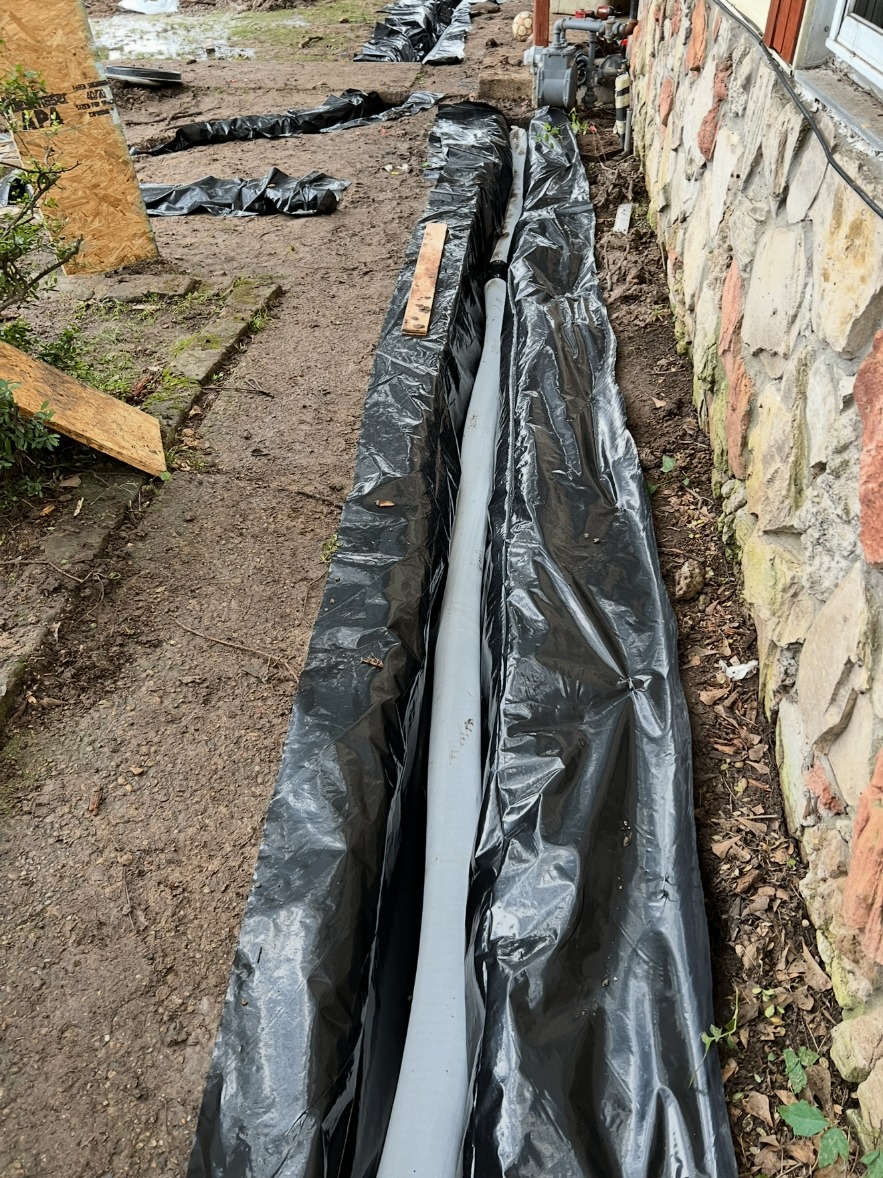 Drain pipe in a lined trench along a stone foundation