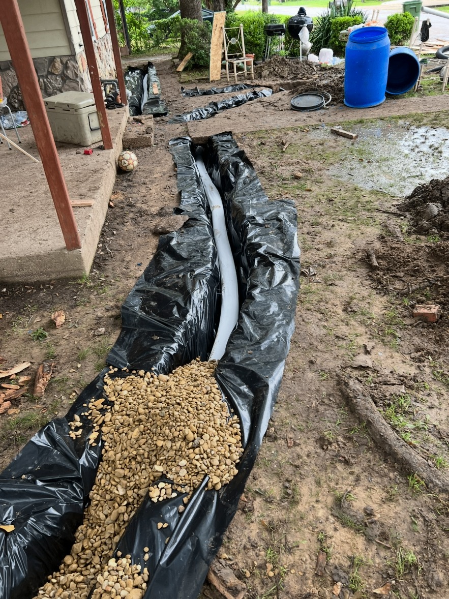Gravel being added over drain pipe in a lined trench