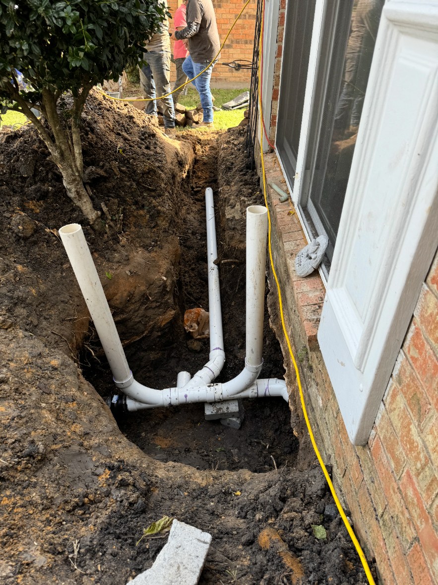 New PVC plumbing lines installed in a trench beside a home's foundation