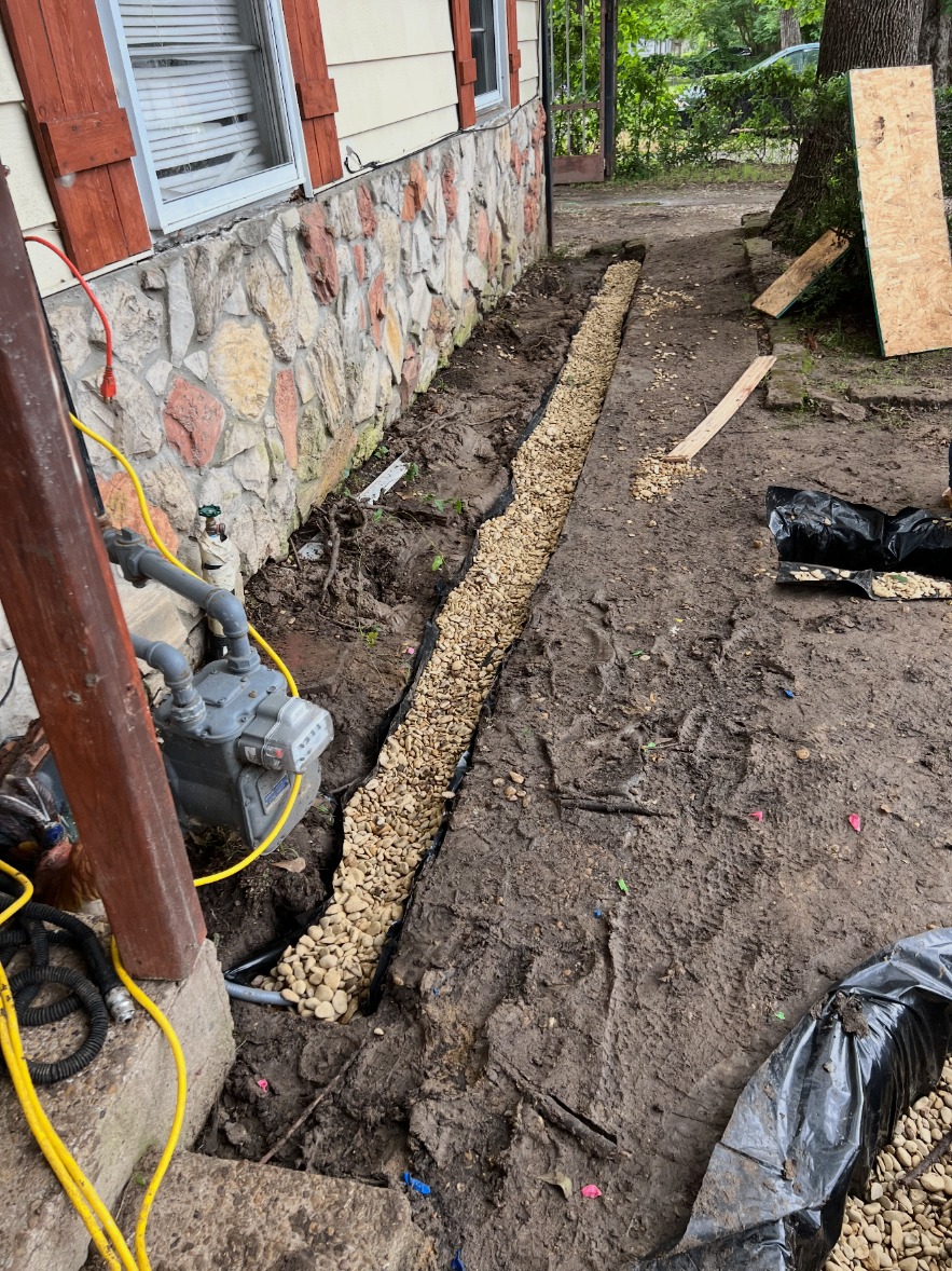 Gravel-filled drain running along a stone foundation