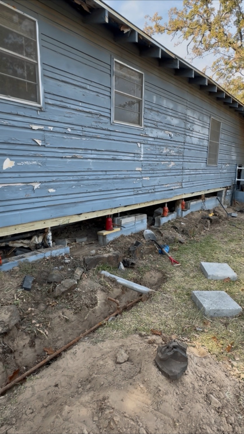 Jacks and block piers along a blue home during leveling