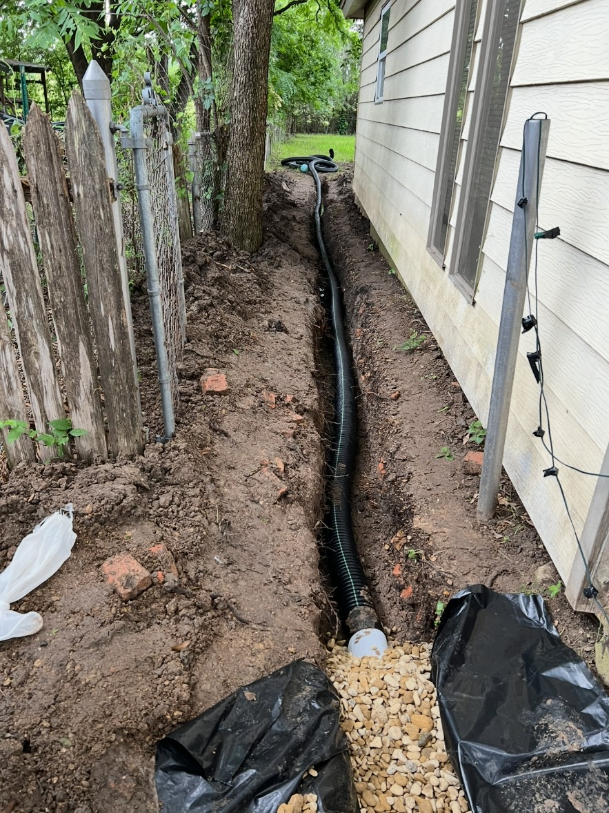 French drain pipe laid in a trench beside a home